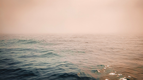 Mystical blue lake waters at sunrise or sunset. A pink sheen falls over the sky and waters creating a beautiful scene. Sunlight glistens on the water and fog fills the atmosphere. Located between Isle Royale and Copper Harbor in the remote Upper Peninsula of Michigan.