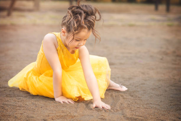 beautiful junior little girl playing in the park in yellow dress laughing with bubbles, screaming with happiness in family enjoying children's day stock photo