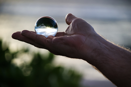 This man’s hand is holding a crystal ball that reflects the ocean.