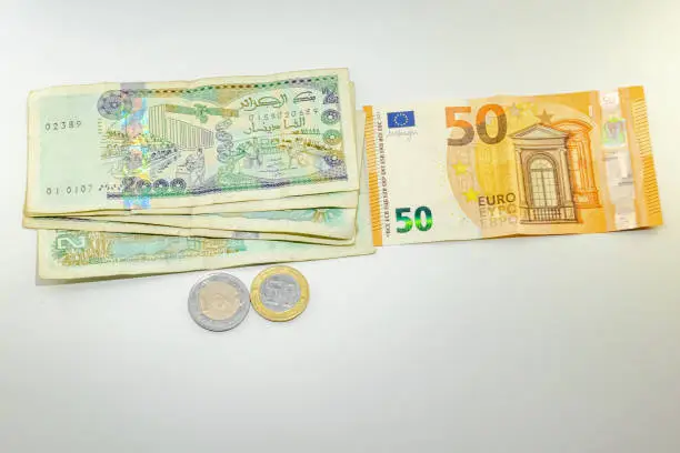 Fifty Euros bill and five bills of two thousand Algerian dinars with a coin of one hundred and a coin of fifty dinars on white background.