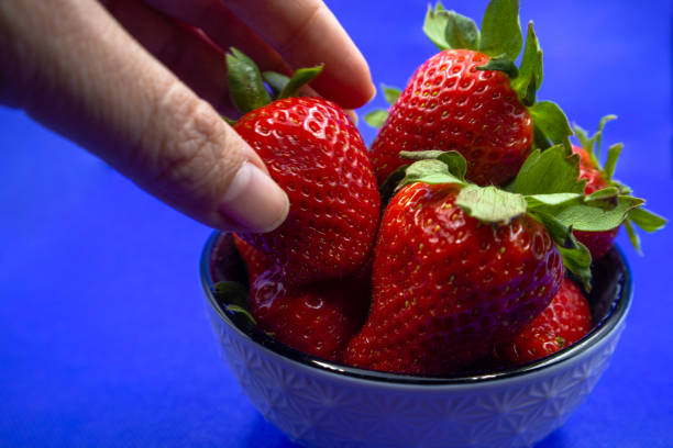istock Person's hand taking a strawberry from a bowl. 1482690620