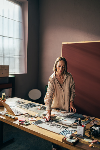 A pensive Caucasian entrepreneur arranging photos on the desk while standing in her office.
