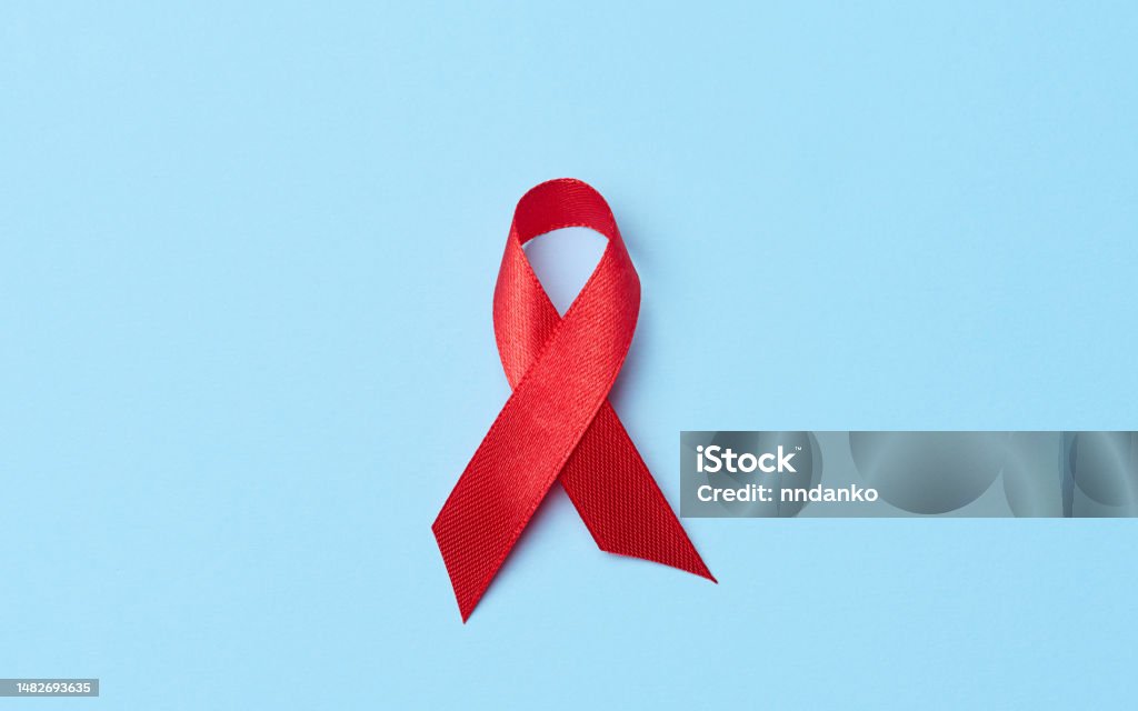 A silk red ribbon in the form of a bow on a blue background, a symbol of the fight against AIDS and a sign of solidarity and support AIDS Stock Photo