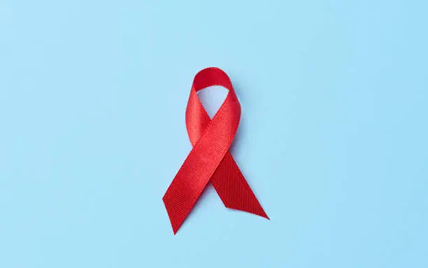 Photo of A silk red ribbon in the form of a bow on a blue background, a symbol of the fight against AIDS and a sign of solidarity and support