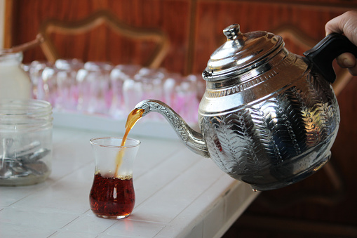 black tea pouring from silver plating teapot with fresh tea leaves, a Glass cup of traditional turkish brewed hot drink