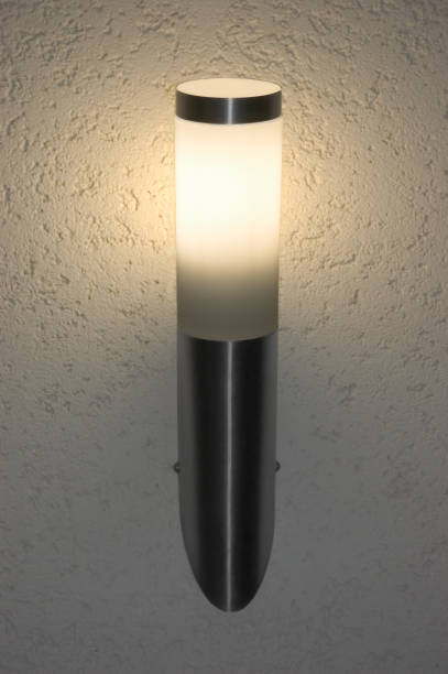 Bright glowing lit inox outdoor wall mounted torch lantern at night, large detailed vertical sconce closeup, light grey textured stucco plaster pattern background shadows, detailed texture