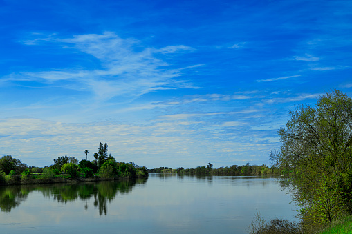 Wide view of the treelined Sacramento River winding it's way south through of the city of Sacramento, under a cloudy sky in the background.\n\nTaken South of Sacramento, California, USA