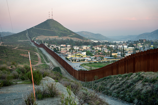 As the sun sets on the International Border Wall at Tecate, Mexico, the towering fence casts a stark shadow across the rugged terrain. The wall, constructed of towering steel slats, stretches into the distance, separating two nations with vastly different cultures and ways of life. The fence glimmers in the fading light, a symbol of the complex and often fraught relationship between the United States and its southern neighbor. Yet, as darkness falls, the wall fades into the background, overshadowed by the natural beauty of the desert landscape and the promise of a new day to come.