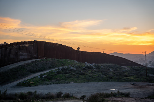 As the sun sets on the International Border Wall at Tecate, Mexico, the towering fence casts a stark shadow across the rugged terrain. The wall, constructed of towering steel slats, stretches into the distance, separating two nations with vastly different cultures and ways of life. The fence glimmers in the fading light, a symbol of the complex and often fraught relationship between the United States and its southern neighbor. Yet, as darkness falls, the wall fades into the background, overshadowed by the natural beauty of the desert landscape and the promise of a new day to come.