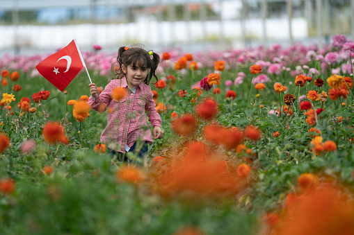 Photo of preschooler girl holding Turkish flag in flower garden celebrating April 23 National Sovereignty and Children's Day, that is Ulusal Egemenlik ve Çocuk Bayramı. Shot under daylight