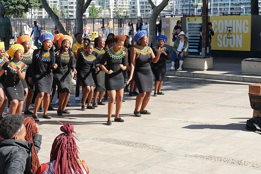 Cape Town, South Africa, 03 26 2023, Street singing and dancing group of African women in traditional dresses entertains tourist passing by in waterfront district in Cape Town during sunny summer day.