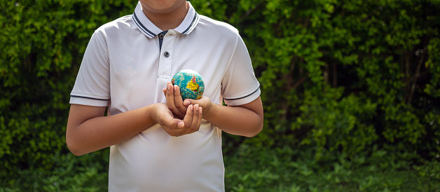 Planet earth in the boy's hands saves and protects the world over blurred green nature background. Environmental concept on Earth Day.