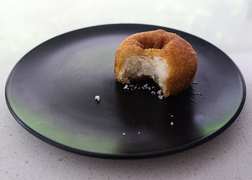 Side view of a donut with a single bite taken out, on a black plate