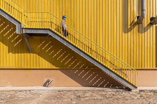 A male worker is walking on the stairs of a yellow factory