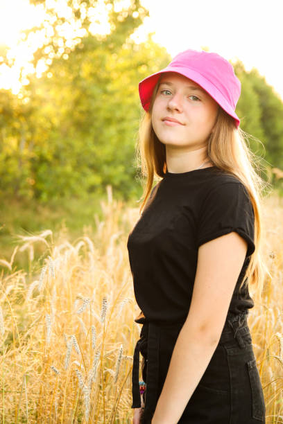 summer teen girl. beautiful smiling teenage girl in dress standing against yellow summer background. high girl 12 or 13 years old on summer lawn. vertical. panama hat. out of focus - 12 13 years pre adolescent child female blond hair imagens e fotografias de stock