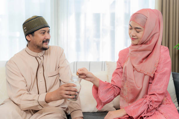 concept financier d’épargne. couple musulman avec pot de pièces de monnaie. une femme met de l’argent dans le bocal en verre étiqueté tenu par un homme - asian tribal culture photos photos et images de collection