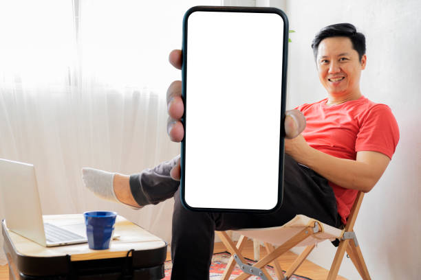 istock Student men resting in his room. Online shopping, home work, freelance, online learning, studying concept. holding a large smartphone with a blank screen 1482714564