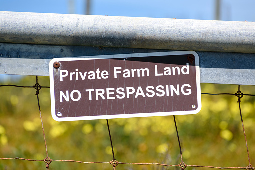Private Farm Land No Trespassing sign posted on a fence. Close up.