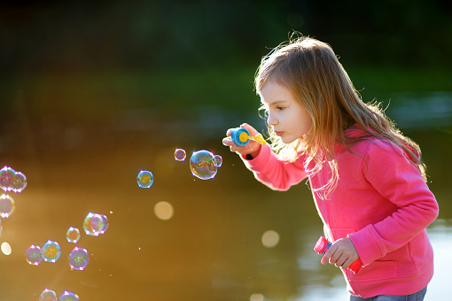 Funny lovely little girl blowing soap bubbles on sunset outdoors
