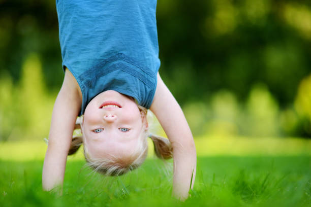 Happy young child playing head over heels on green grass in spring park