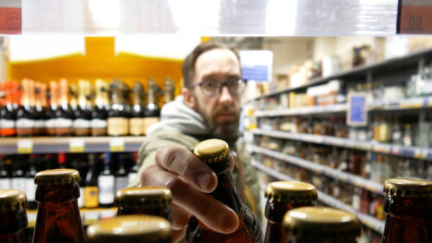 Close-up of many beer bottles on a store shelf and a bearded man with glasses taking one stock photo