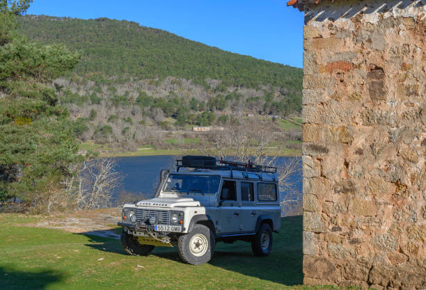 A white land rover defender 110 prepared for an overland trip, standing on the grass, in the shadow of the old stone wall of a hermitage in Spain, on the shore of a lake, in the background a mountain, above the clear blue sky without clouds A white land rover defender 110 prepared for an overland trip, standing on the grass, in the shadow of the old stone wall of a hermitage in Spain, on the shore of a lake, in the background a mountain, above the clear blue sky without clouds horizon over land stock pictures, royalty-free photos & images