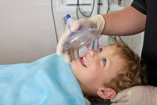 fotografii de stoc, fotografii și imagini scutite de redevențe cu băiatul curajos zâmbește și se uită la medic înainte de operație pe masa de operație - anestezic