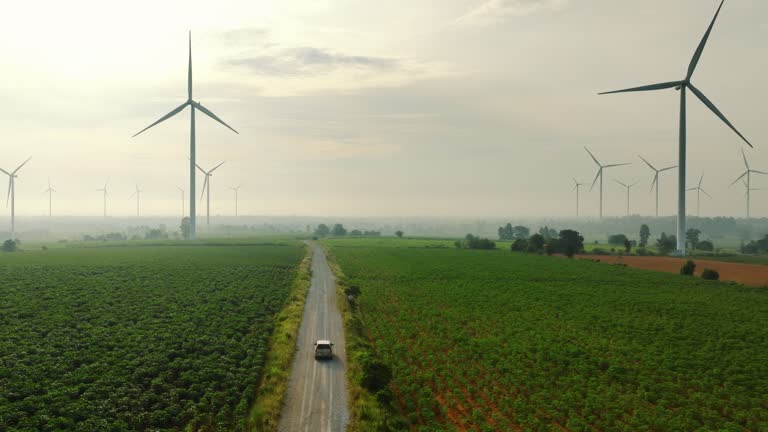 Aerial view of car driving through green field surrounded by wind turbines.