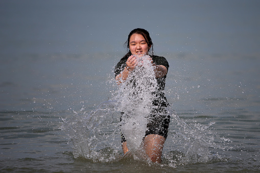 An Asian teenage girl is enjoying splashing sea water by the beach