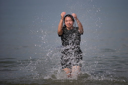 An Asian teenage girl is enjoying splashing sea water by the beach