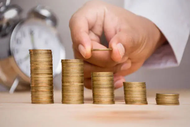 Hand stacking gold coins with seedlings are growing on coins laid out and blurred clock background .Business Finance and Money concept,Save money for prepare in the future,productivity growth concept