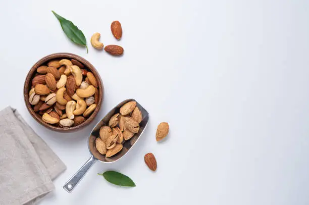 nuts almonds and cashews are placed in a wooden bowl and a metal scoop with napkin on a light gray background. Top view,  flat lay and copy space