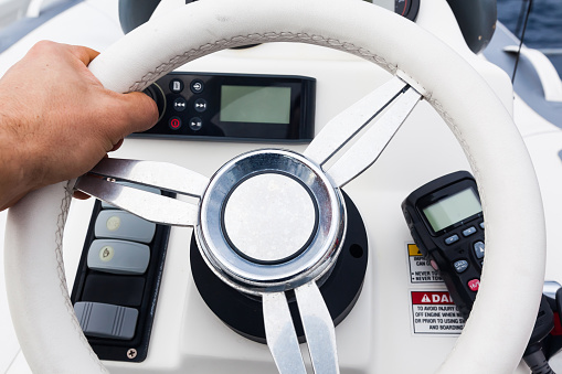 Hand on the control panel of a motorboat. Steering wheel, gear levers and control buttons.