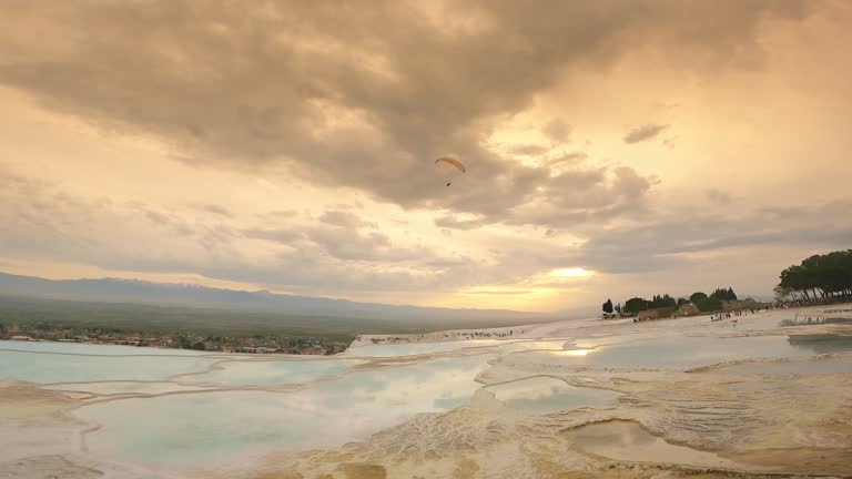 Paraglider is flying  over  travertine pools and Hierapolis in Pamukkale during stunning sunset sky in Denizli