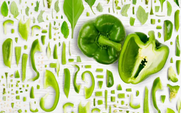 Abstract background made of Green Pepper vegetable pieces, slices and leaves on wooden background.