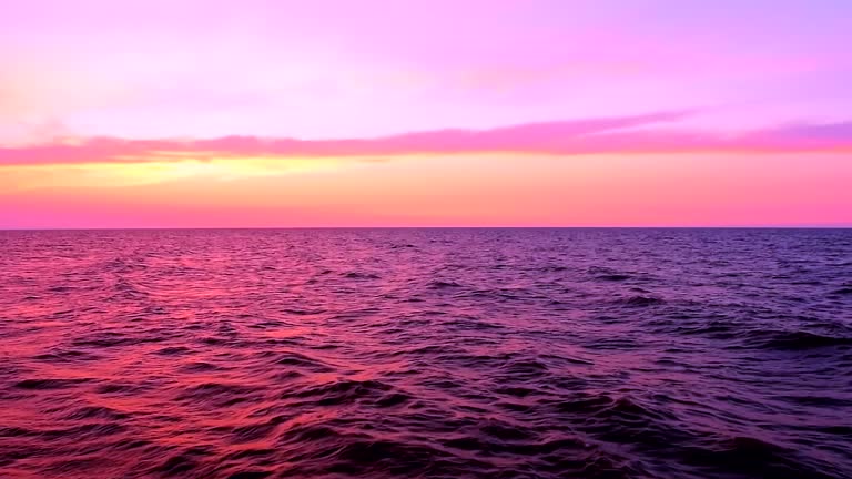 Sea waves with reflection of pink and purple sunset light on the pink and purple sunset sky background, slow motion, hd. ProRes 422 HQ.