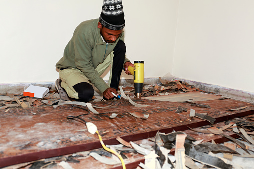 Carpenter removing old varnish from wood using scraper and heat gun at his workshop portrait Indoor.