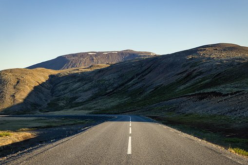 The way forward - empty country road in the late evening sun light through rural hill landscape under blue summer sky leading towards a strong road curve in the shade of the southern icelandic hills Route 1, South-East Iceland, Nordic Countries, Northern Europe