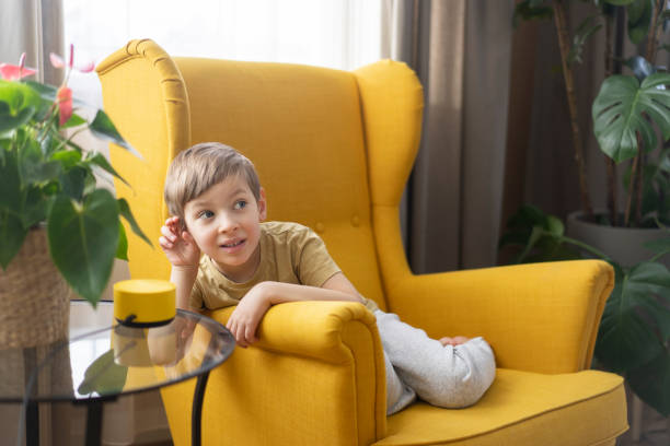 A little boy sits in a chair and communicates with a smart speaker. Child with smart column, modern technology