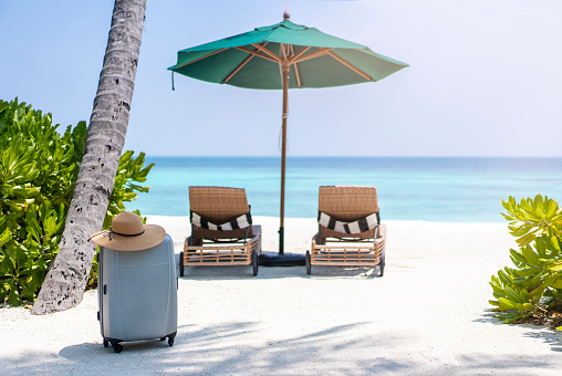 A suitcase and a straw hat against the backdrop of the landscape of the Maldives. Travel and tropical vacation concept.