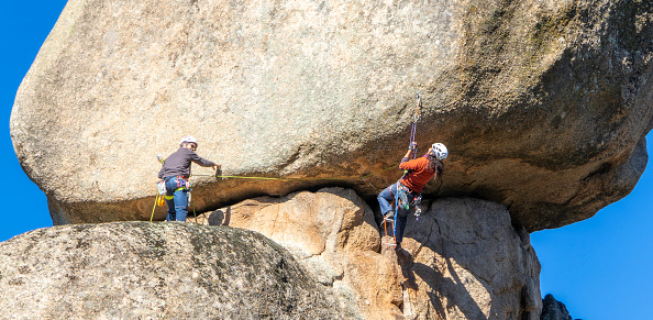 two young adults working together to climb a granite wall. Rock climbing. Extreme sports concept