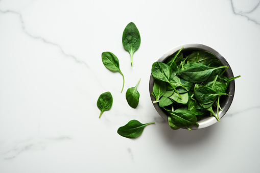 A bunch of Fresh baby spinach leaves in the in a stainless steel bowl on white marble background. High quality photo