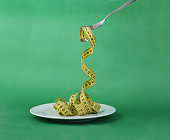 Fork with measuring tape on green background. Healthy eating and dieting concept.