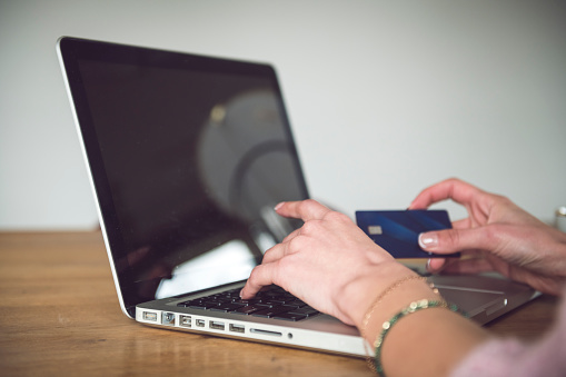 Shot of a woman holding her credit card while sitting at home with her laptop