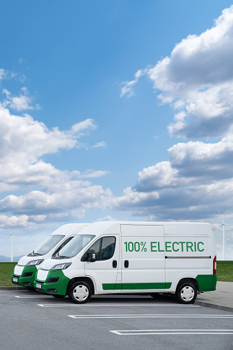 Electric vans parked in a row. Wind turbines in a horizon