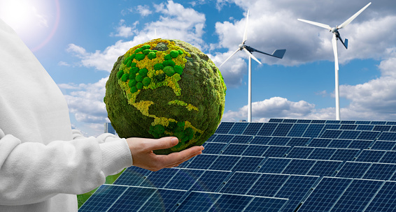 Woman holding a green planet Earth on a background of wind turbines and solar panels. Symbol of sustainable development and renewable energy