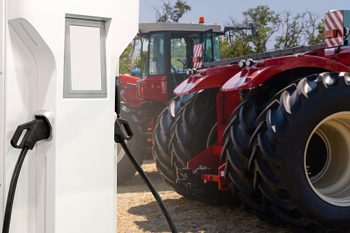 Electric vehicles charging station on a background of agricultural tractors. Concept