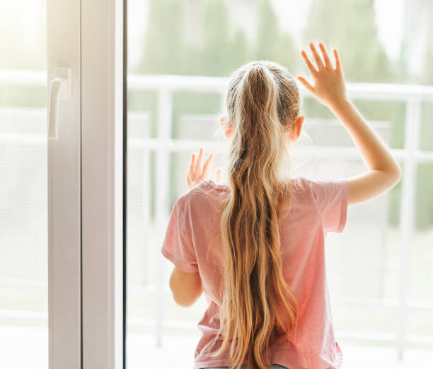 istock Sad little girl looking through  window at home. 1482768167
