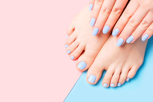 Female hands and feet with light blue manicure and pedicure on a blue and pink background top view close up.