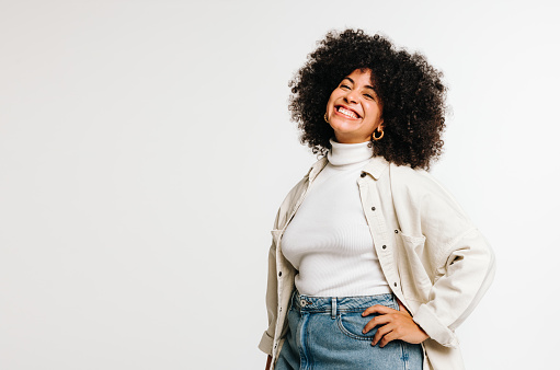 Carefree woman with Afro hair smiling at the camera while standing against a studio background. Beautiful young woman of colour wearing her natural hair with pride.